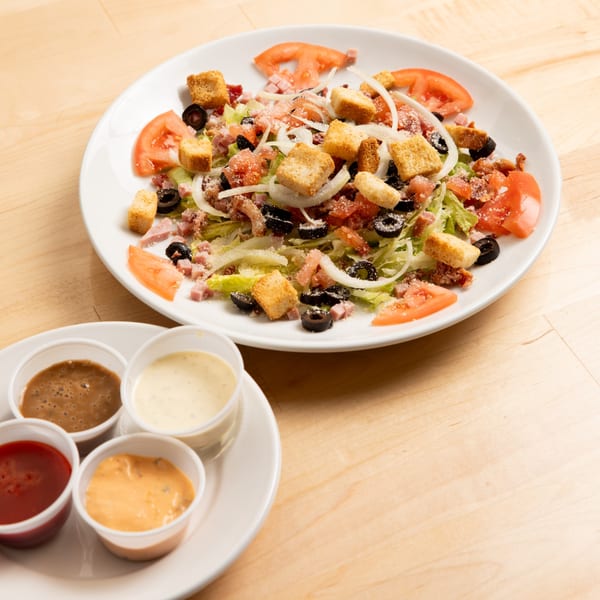 Bronko's Pizza salad with lettuce, tomatoes, olives, ham, croutons, and onions, with four dressings.